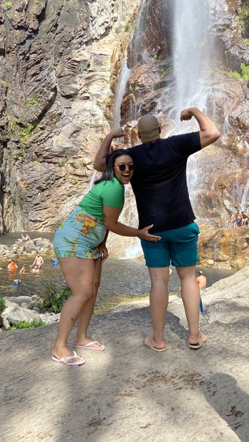 Ana e Arthur fazendo poses diante de uma cachoeira.